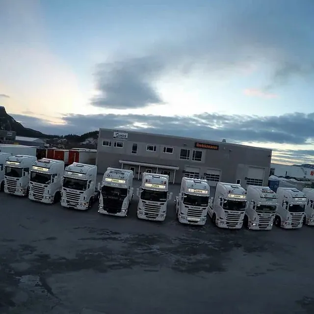 Rekke med lastebiler parkert utenfor transportselskapets terminal og administrasjonsbygg.