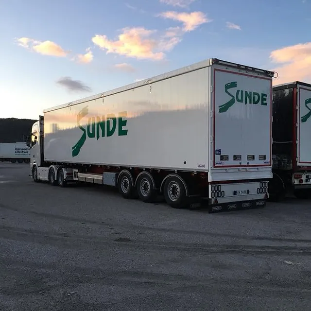 Semitrailer med firmaprofilering parkert på terminalområde i kveldslys under klar himmel.