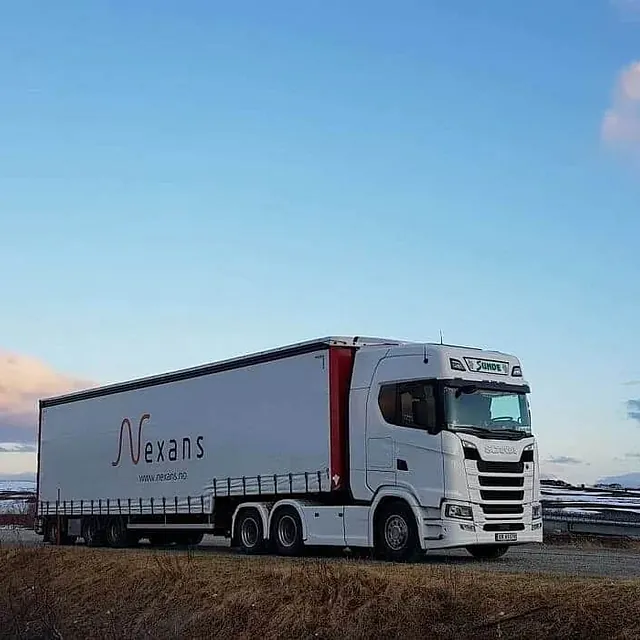 Vogntog parkert i åpent vinterlandskap med snøflekker og vid horisont under kveldshimmel.