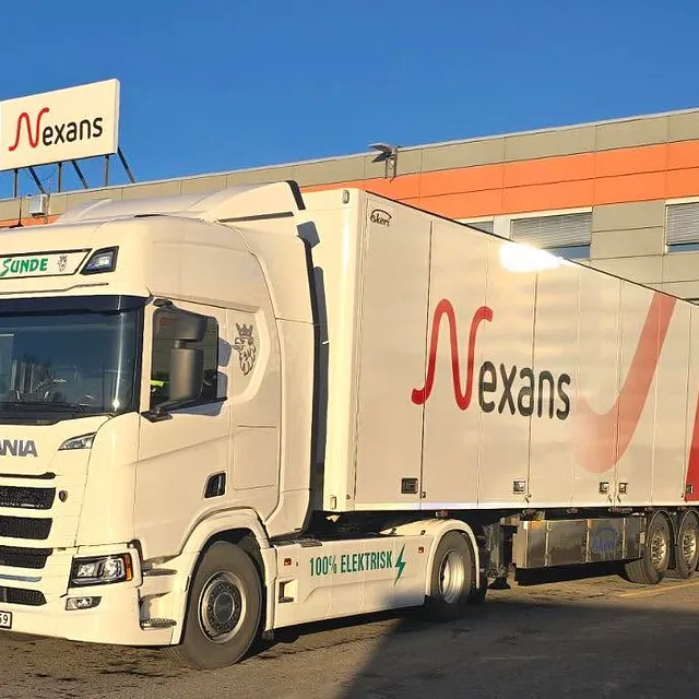 Elektrisk lastebil laster ved fabrikk med Nexans-logo og tilkoblet semitrailer.
